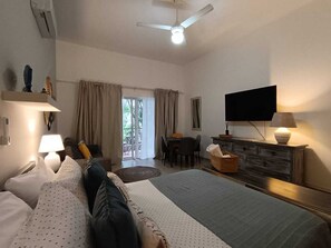A hotel room with a bed, a desk, a chair, a television, and a ceiling fan. - Fastastico Apt. Al Cadaques villa and Resort (BAYAHIBE)