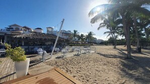 A beachside hotel with a thatched-roof bar, outdoor seating, and palm trees. - Fastastico Apt. Al Cadaques villa and Resort (BAYAHIBE)