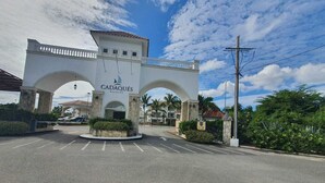 A large arched entrance with the name 'CADAQUÉS' and a sailboat logo, surrounded by greenery and palm trees. - Fastastico Apt. Al Cadaques villa and Resort (BAYAHIBE)