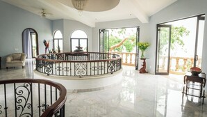 Un'ampia stanza con pavimento in marmo, una scala a forma di spirale con ringhiera, un lampadario e grandi finestre con vista sul verde.