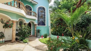 Un cortile con una fontana, un balcone e rigogliosa vegetazione tropicale.