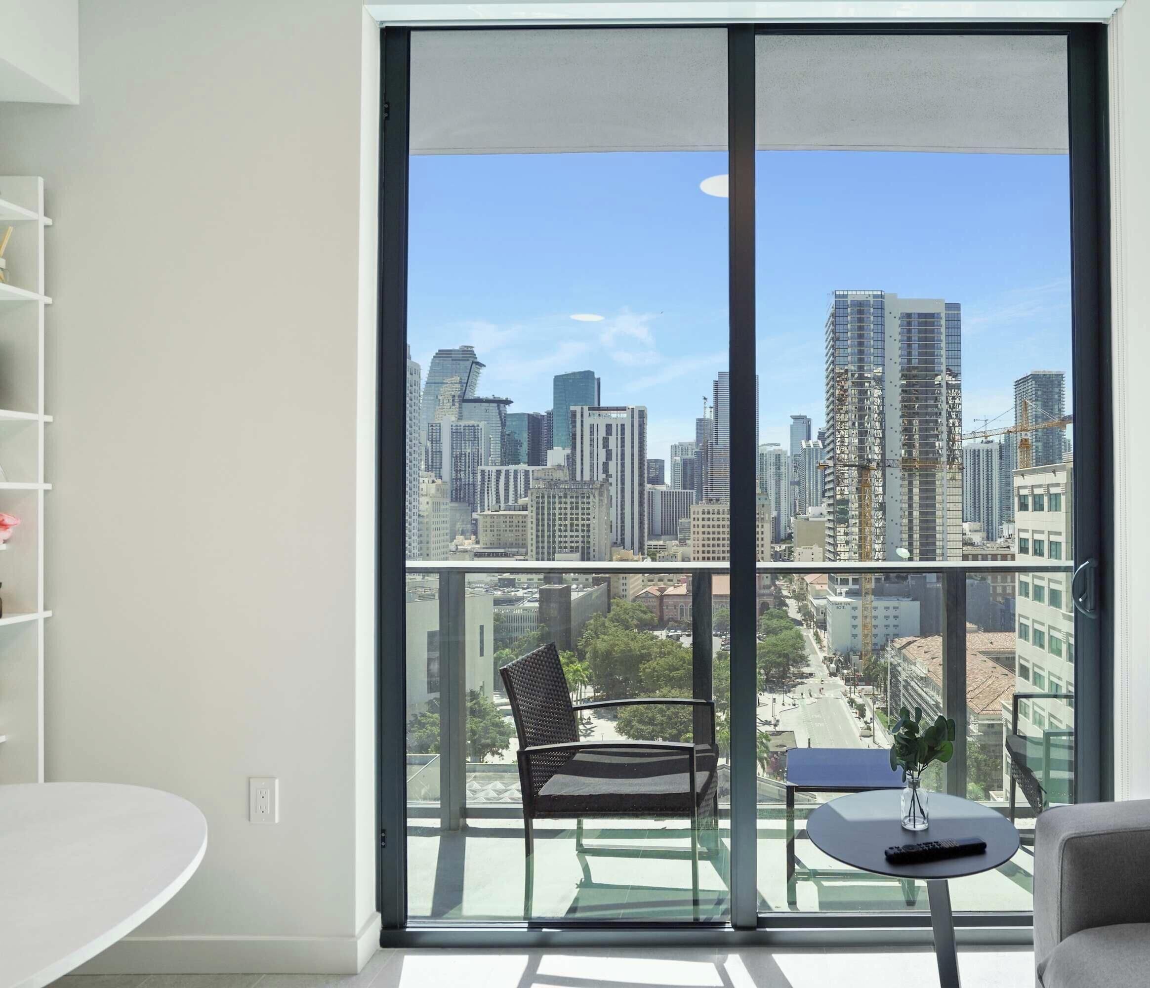 A modern apartment with a large balcony, a white round table, a black chair, and a small potted plant.