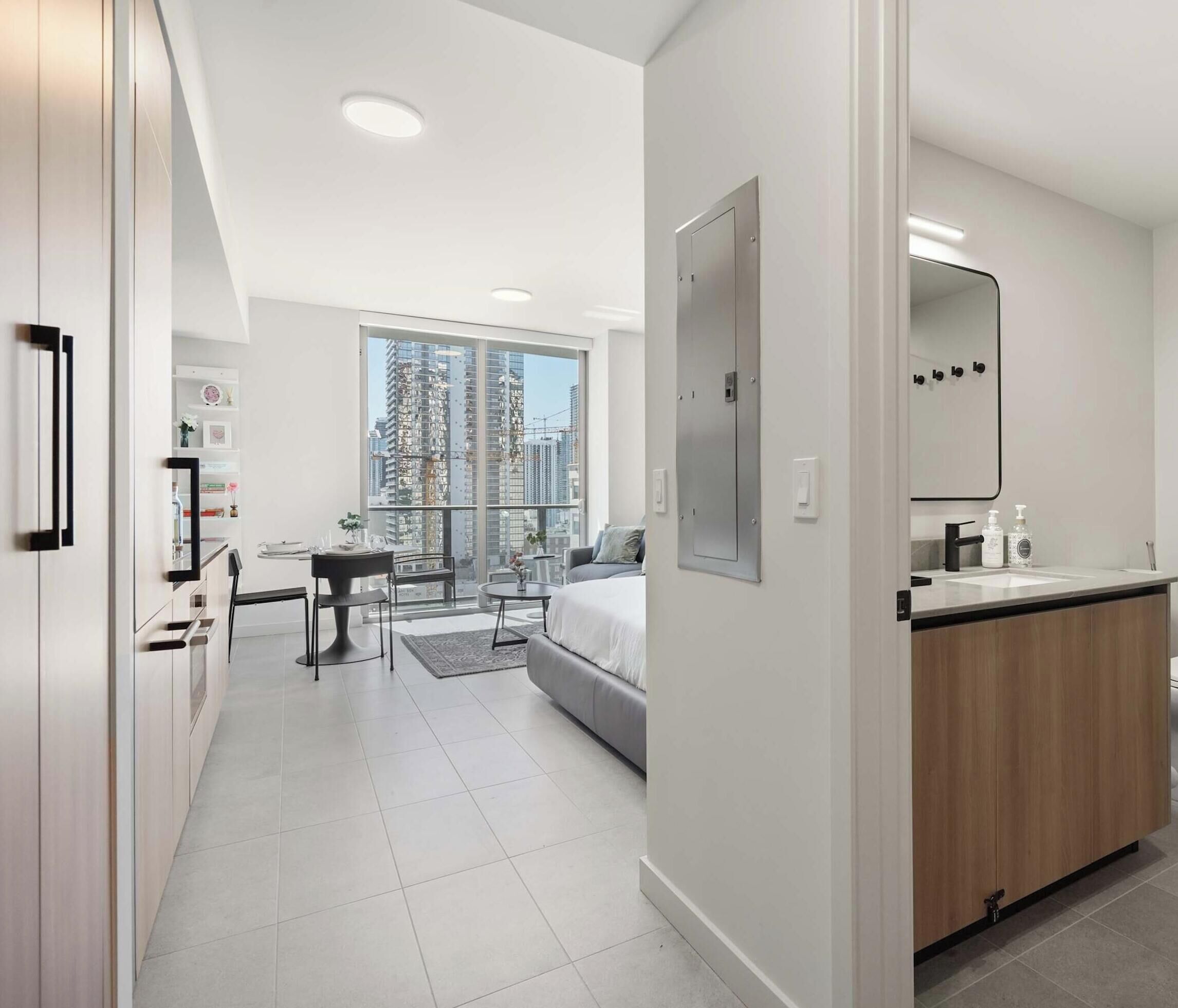 Una habitación de hotel moderna con balcón, cama, escritorio y baño con espejo y lavamanos.