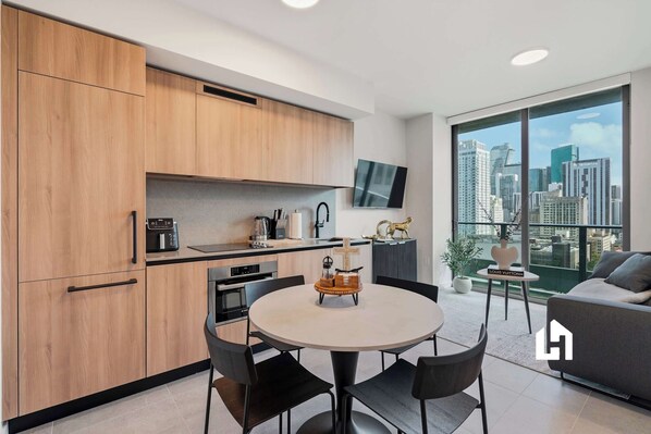 A modern kitchen with wooden cabinets, a dining area with a round table, and a city view through large windows. - Skyline View Condo in the Heart of Miami (Miami)