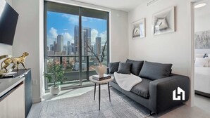 Uma sala de estar moderna com sofá, uma mesinha, uma planta em vaso e vista para a cidade através de grandes janelas.