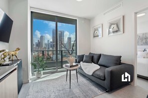 A modern living room with a sofa, a small table, a potted plant, and a city view through large windows. - Skyline View Condo in the Heart of Miami (Miami)