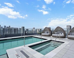 Ein Pool auf dem Dach mit Blick auf die Stadt, drei Korbstühle und ein Gebäude mit der Aufschrift 'RENT 305'.