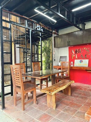 A restaurant with a glass-top table, wooden chairs, a bench, and a red wall with a sign. - Soulelle Villa with Pool (Silang)