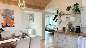 Eine moderne Küche mit Holzboden, ein Essbereich mit Tisch und Stühlen sowie eine Wohnarea mit Sofa und Kaffeemaschine.