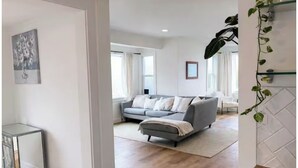 Ein modernes Wohnzimmer mit einem grauen Sofa, einem kleinen Beistelltisch und einem großen Spiegel.