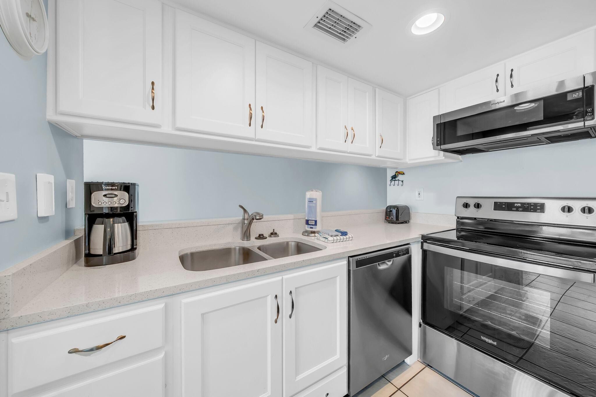 A modern kitchen with white cabinets, stainless steel appliances, a built-in oven, and a coffee maker.
