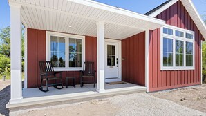 A red building with a porch, two rocking chairs, and a door. - The Cherry Cottages (Fish Creek)