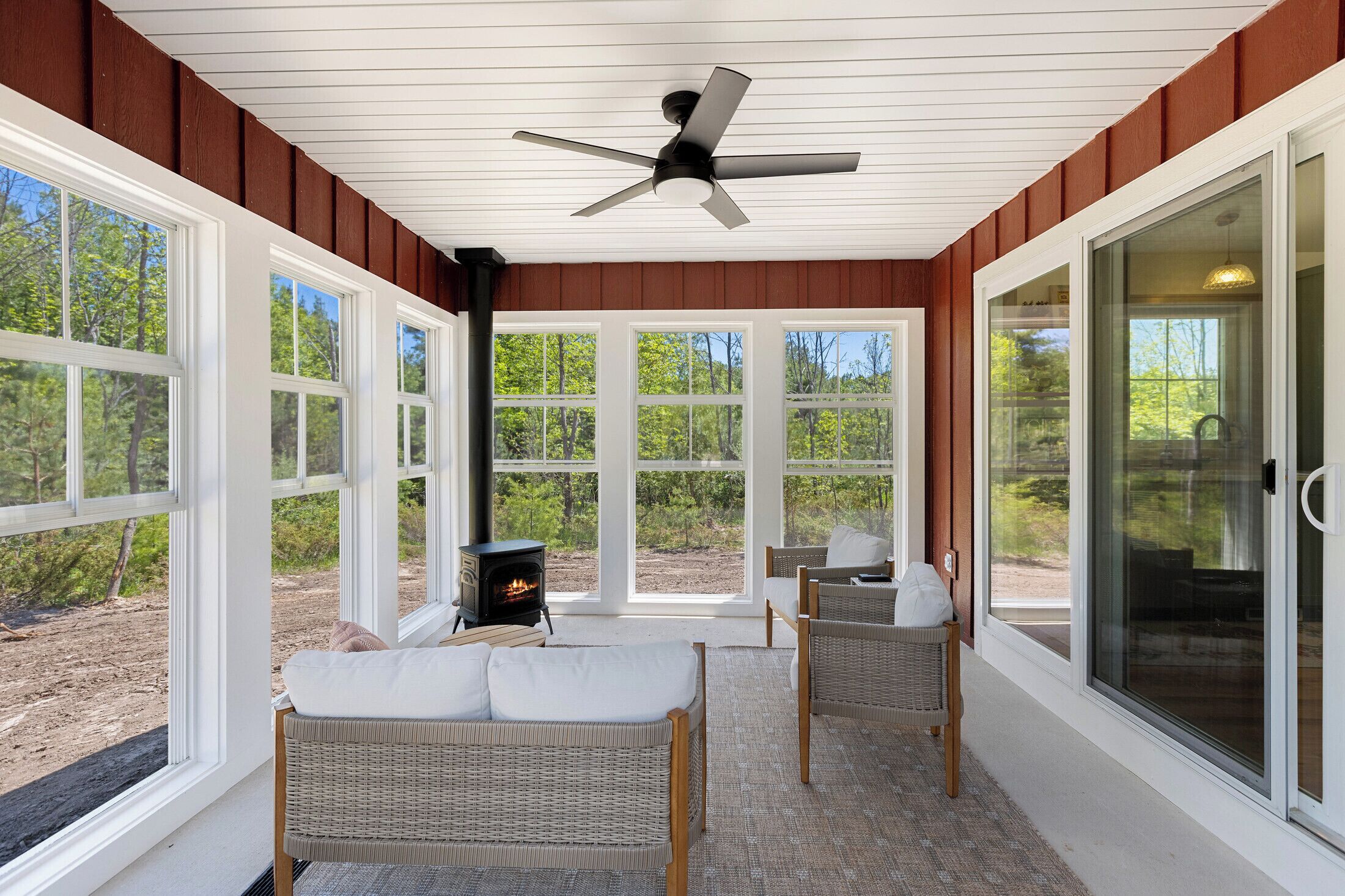 A covered outdoor seating area with wicker furniture, a ceiling fan, and a wood-burning stove.