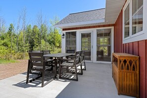 A patio with a table and chairs, a wooden cabinet, and a building with a red exterior and large windows. - The Cherry Cottages (Fish Creek)