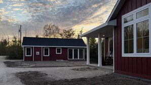 A red building with a covered porch and a gravel driveway. - The Cherry Cottages (Fish Creek)