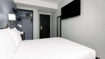 Une chambre d’hôtel avec un grand lit, un téléviseur à écran plat fixé au mur, une table de chevet avec une lampe et une petite étagère avec une radio et un vase de fleurs.