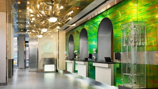 A reception area with a modern design, including a unique chandelier, a green wall with a textured pattern, and a reception desk with a glass display case.