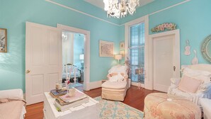 Quarto com parede verde-água, um candelabro, uma porta branca e uma cadeira branca com almofada.