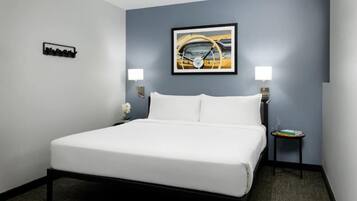 A hotel room with a bed, two bedside lamps, a framed picture on the wall, a small table with a book, and a flower on the bedside table.