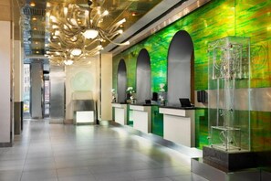 Ett välkomnande område med modern design, inklusive en unik kristallkrona, en grön vägg med ett mönstrat utseende och en receptionsdisk med ett glasmontrinskåp.