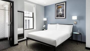 A hotel room with a bed, a nightstand with a lamp, a framed picture on the wall, and a window.