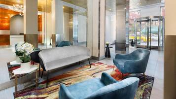 Eine moderne Lobby mit einer Rezeption, einer Couch, zwei Sesseln und einem farbenfrohen Teppich.