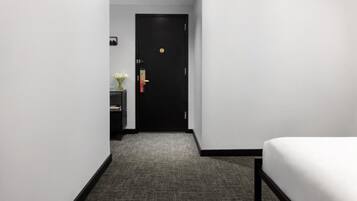 Une chambre d’hôtel avec un lit, un bureau agrémenté d’un vase de fleurs et une porte dotée d’une serrure.