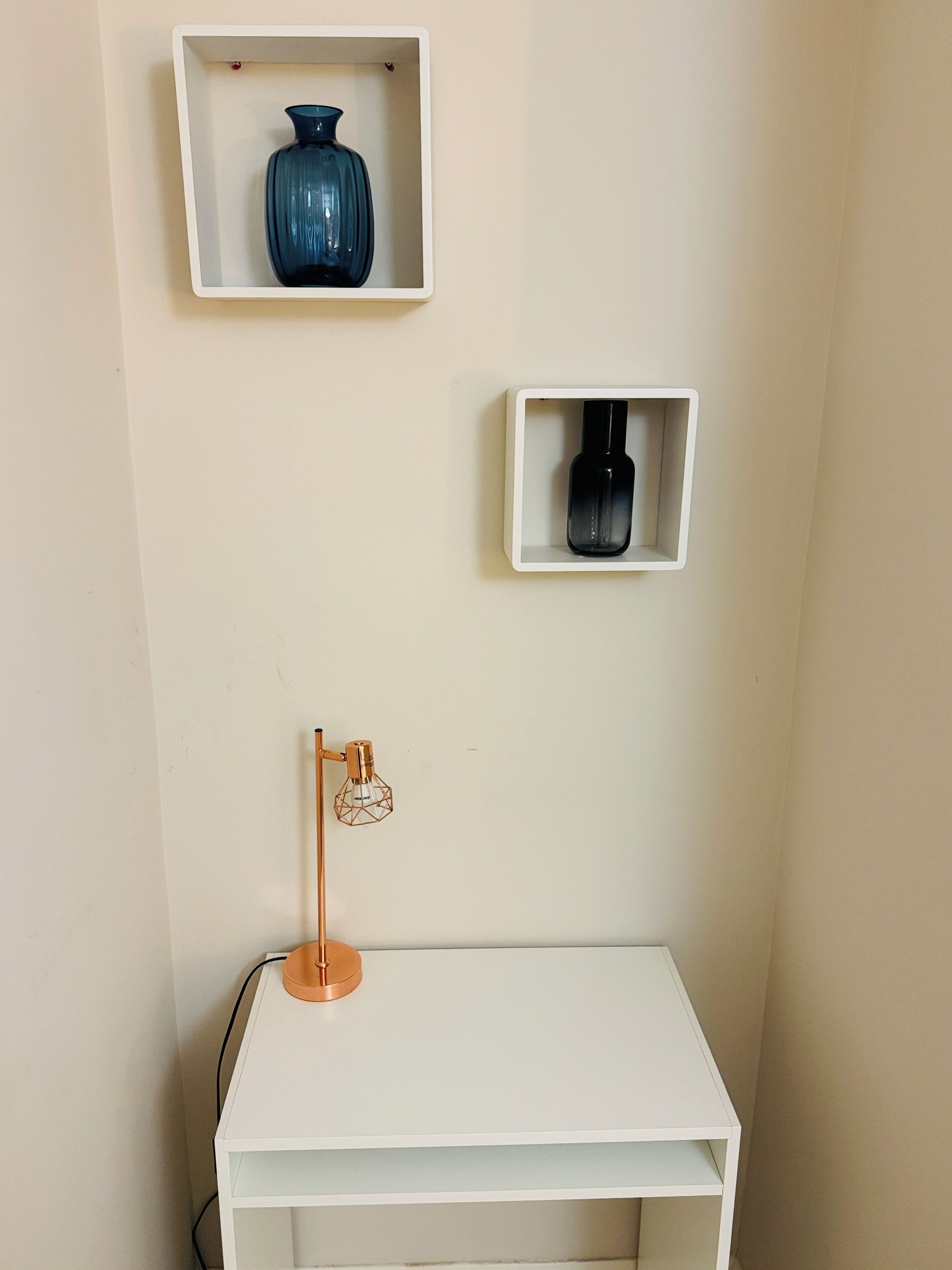 Ein weißer Schreibtisch mit einer Lampe und zwei Regalen mit Vasen.