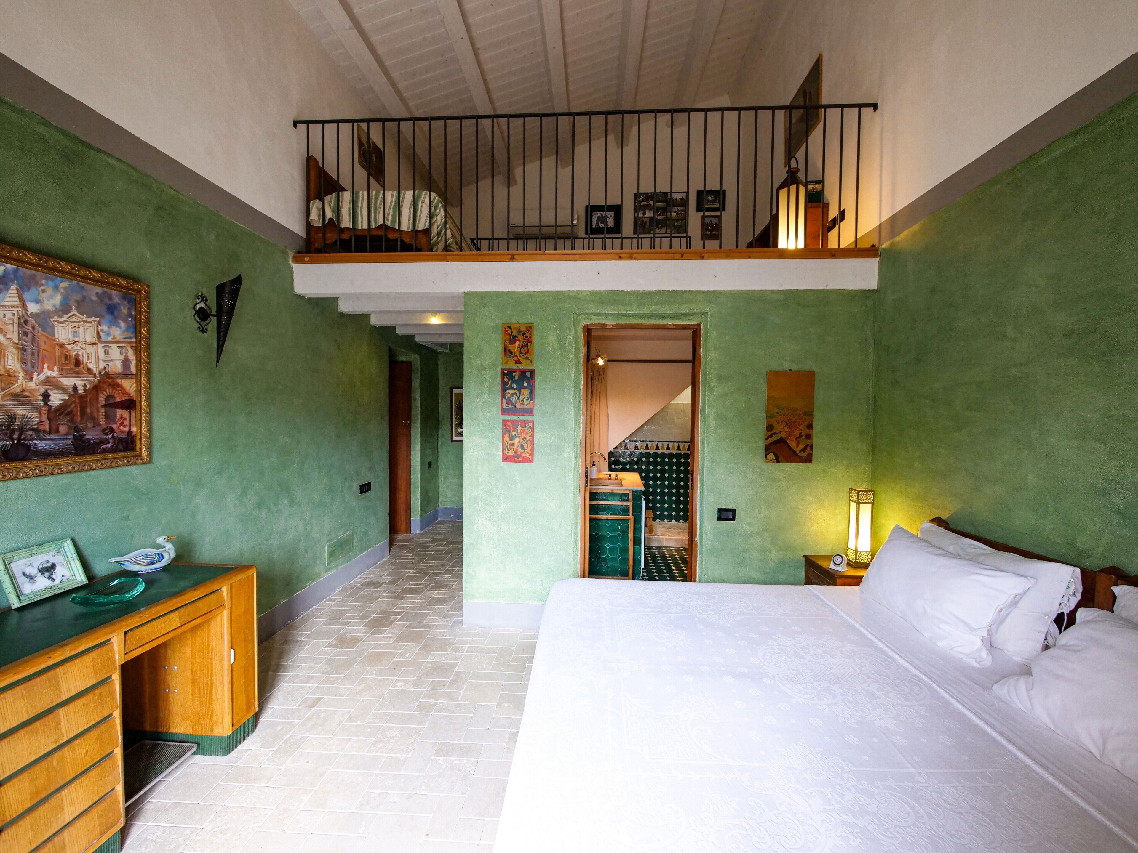 Een slaapkamer met een bed, een bureau, een balkon en een trap naar een hoger gelegen niveau.