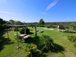 Un espace aménagé au bord de la piscine, avec des chaises longues, une pergola et une vue sur un paysage naturel.