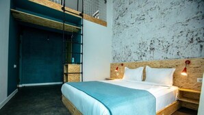 A bedroom with a bunk bed, a wooden headboard, a blue bedspread, and a wall-mounted shelf.