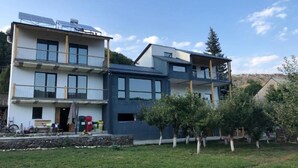 Un edificio residencial moderno de varios pisos con balcones, paneles solares y un jardín bien cuidado.