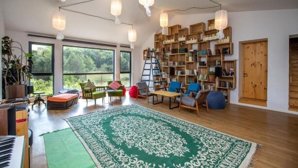 Un salón amplio con un tapete verde grande, estanterías de madera y un piano.
