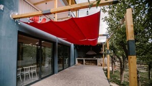 Un espacio de patio al aire libre con un toldo rojo, puertas de vidrio que dan a un comedor y un suelo de piedra.