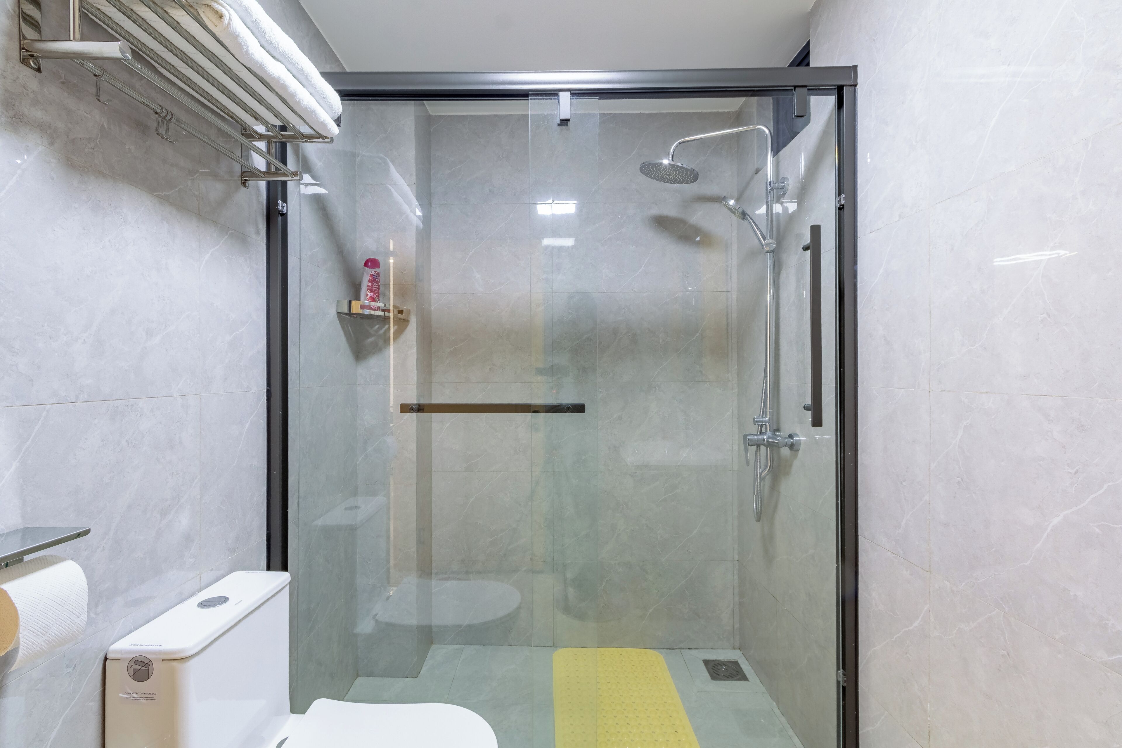 A glass-enclosed shower stall with a handheld showerhead, a towel rack, and a toilet paper dispenser.