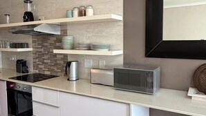 Una cocina moderna con armarios blancos, estufa integrada, microondas y cafetera.