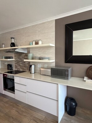 A modern kitchen with white cabinetry, a built-in stove, a microwave, and a coffee maker. - A cosy retreat, a walk away from Big bay with Table mountain in the horizon (Cape Town)