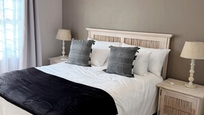 Un dormitorio con cama, mesitas de noche, ventana con cortinas y aire acondicionado.