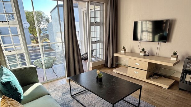 Una sala de estar moderna con sofá, mesa de centro, televisor y puerta corrediza de vidrio.