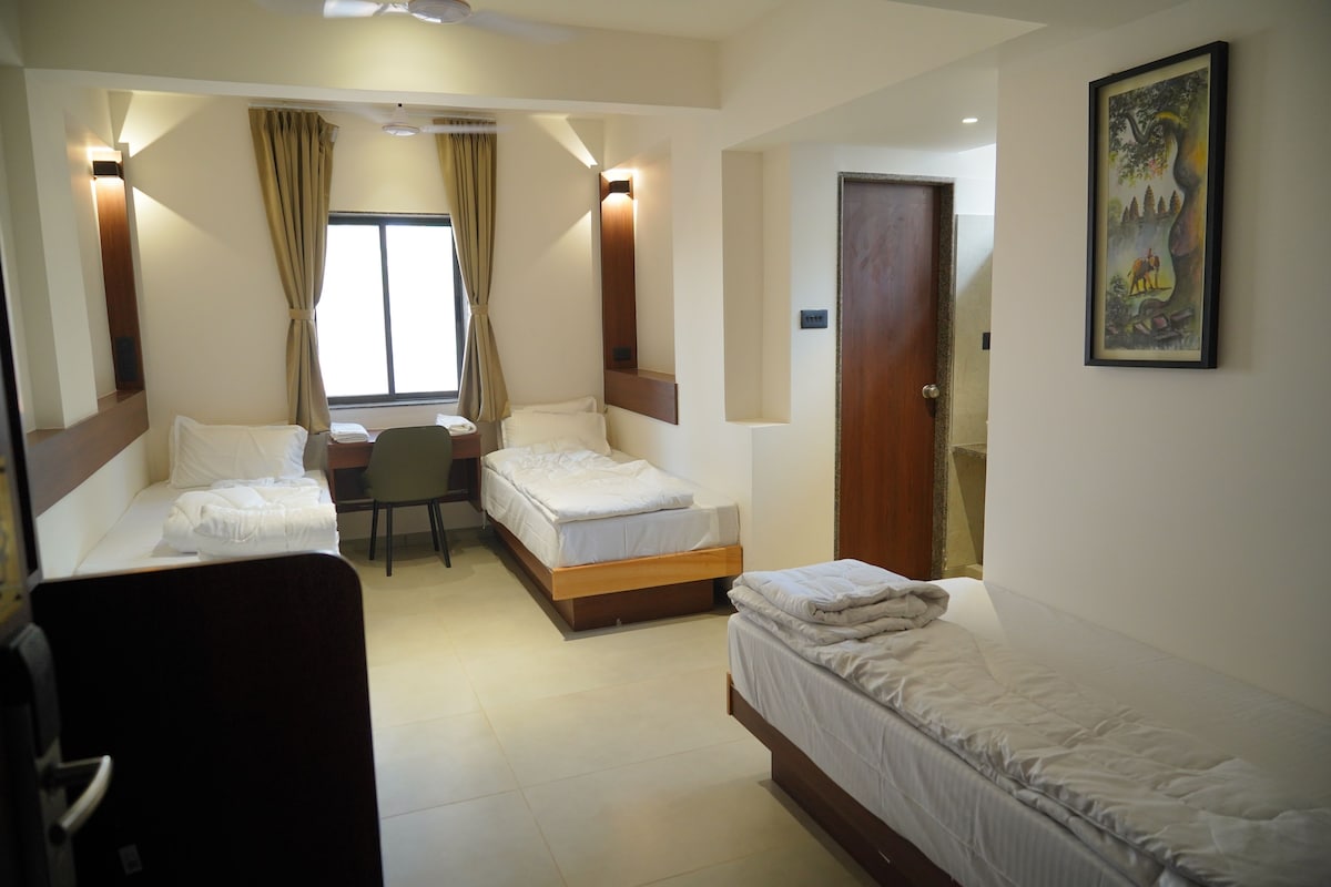 A hotel room with two single beds, a desk, a chair, and a large window with curtains.