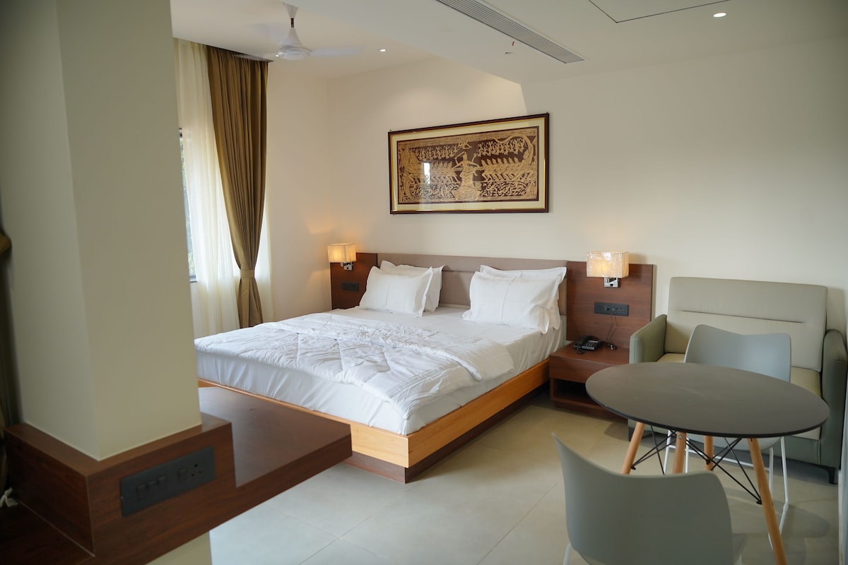 A hotel room with a bed, bedside lamps, a desk, a chair, and a table.