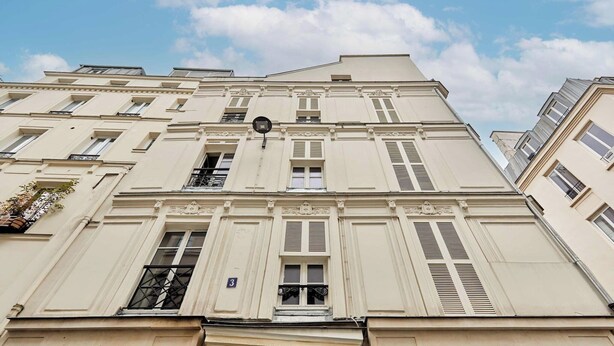 Un edificio de varias plantas con un estilo arquitectónico clásico, que presenta ventanas simétricas, contraventanas y molduras decorativas.