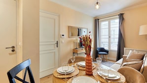 Un comedor con una mesa preparada para cuatro, un jarrón con flores y vistas a la ciudad a través de amplias ventanas.