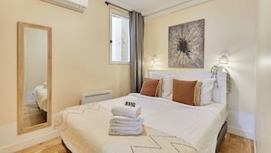 Habitación de hotel con cama, un espejo grande, una ventana con cortinas, aire acondicionado instalado en la pared y un adorno mural.