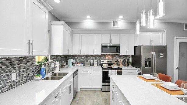 A modern kitchen with white cabinets, a black and gray backsplash, stainless steel appliances, and pendant lighting. - Urban Townhome in Central Houston - near NRG Stadium! (Houston)