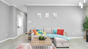 A modern living room with a grey wall, a beige sofa, a wooden coffee table, and a colorful rug. - Urban Townhome in Central Houston - near NRG Stadium! (Houston)