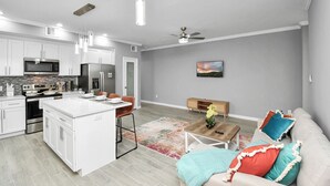 A modern kitchen with white cabinetry, a central island, and stainless steel appliances. There is a dining area with a table and chairs, and a living room with a sofa and a coffee table. - Urban Townhome in Central Houston - near NRG Stadium! (Houston)