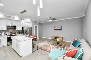 A modern kitchen with white cabinetry, a central island, and stainless steel appliances. There is a dining area with a table and chairs, and a living room with a sofa and a coffee table. - Urban Townhome in Central Houston - near NRG Stadium! (Houston)