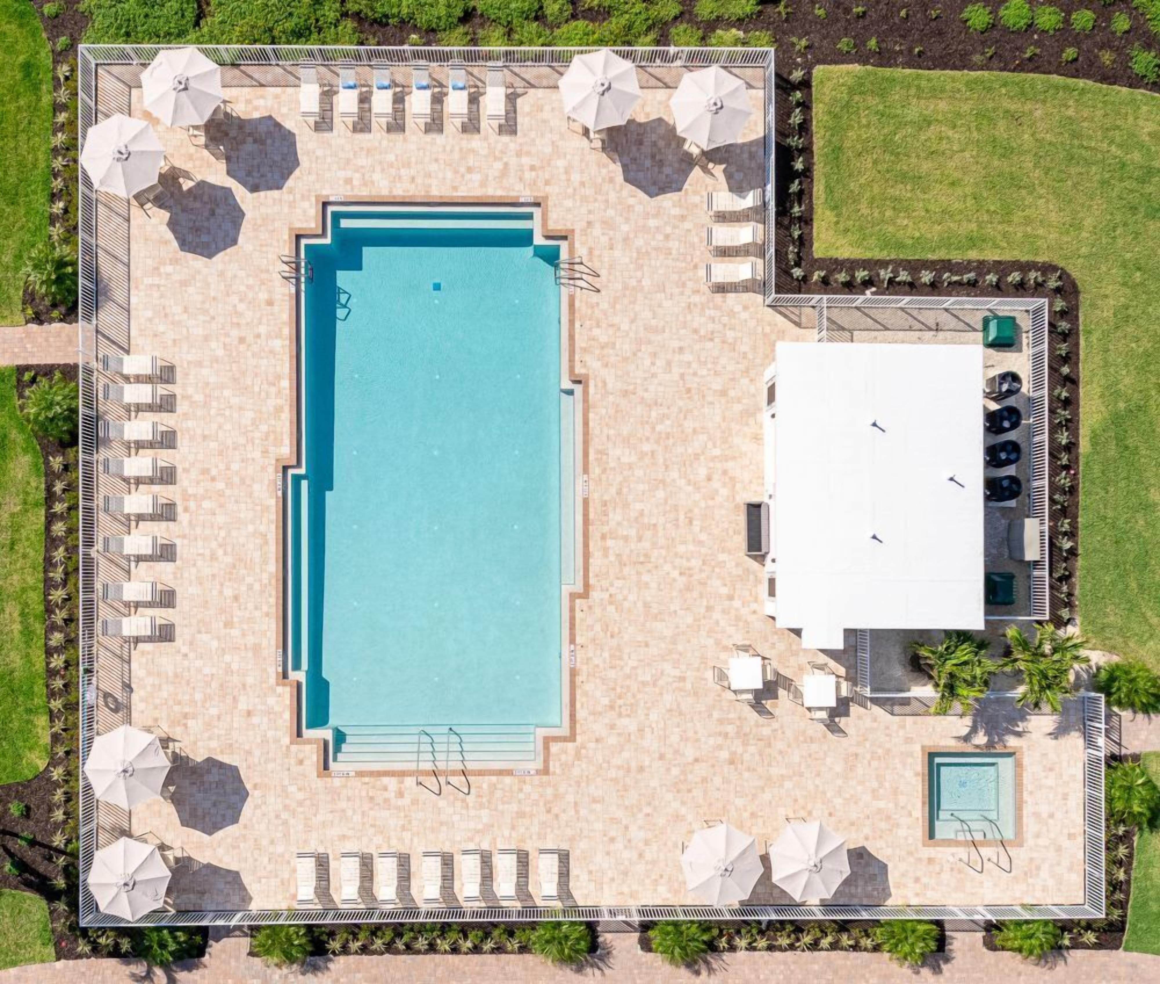 Vista aérea de una zona de piscina con tumbonas, sombrillas y una piscina separada.