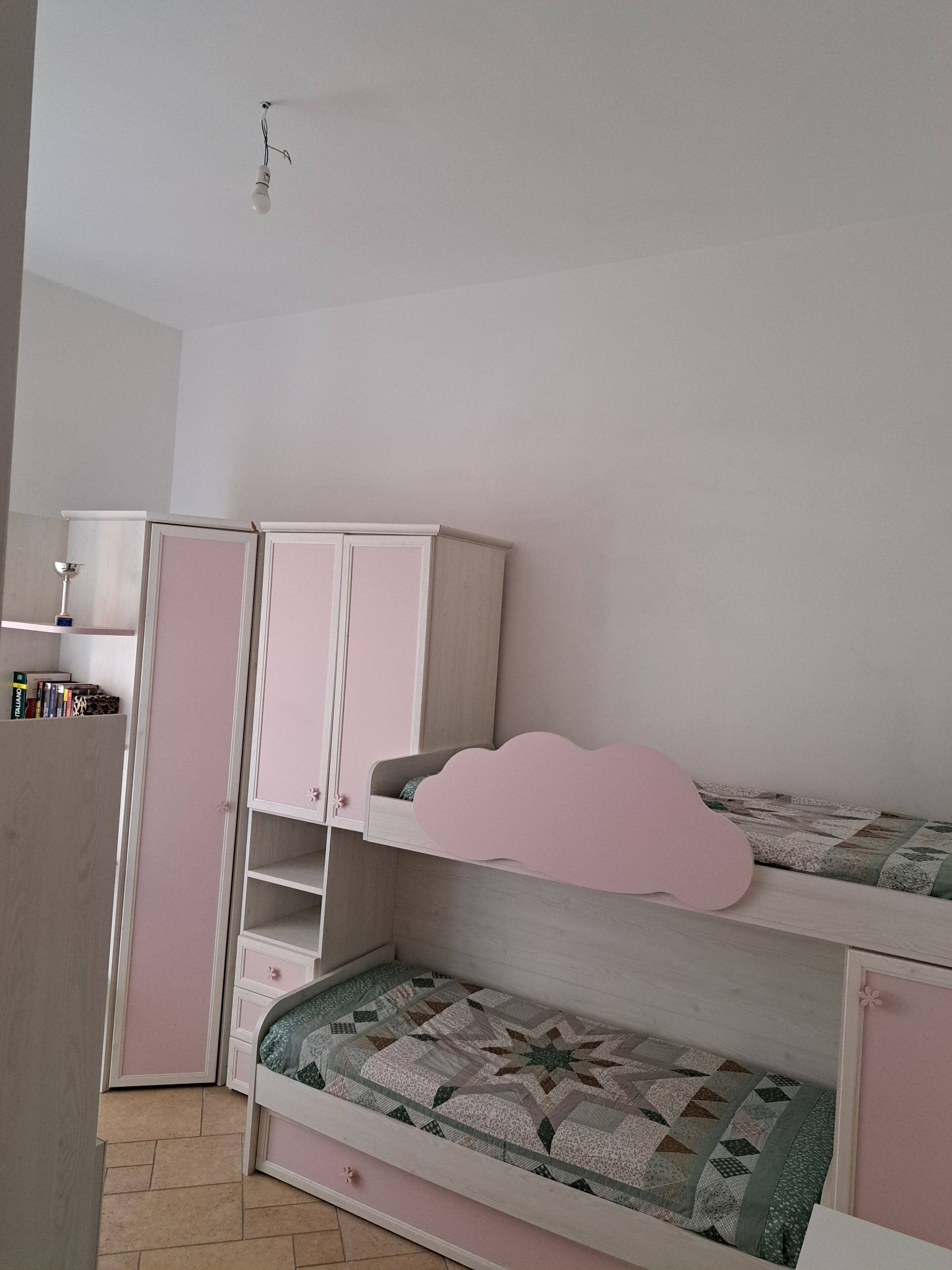 Une chambre d’enfant avec des lits superposés, une armoire et une petite étagère remplie de livres.